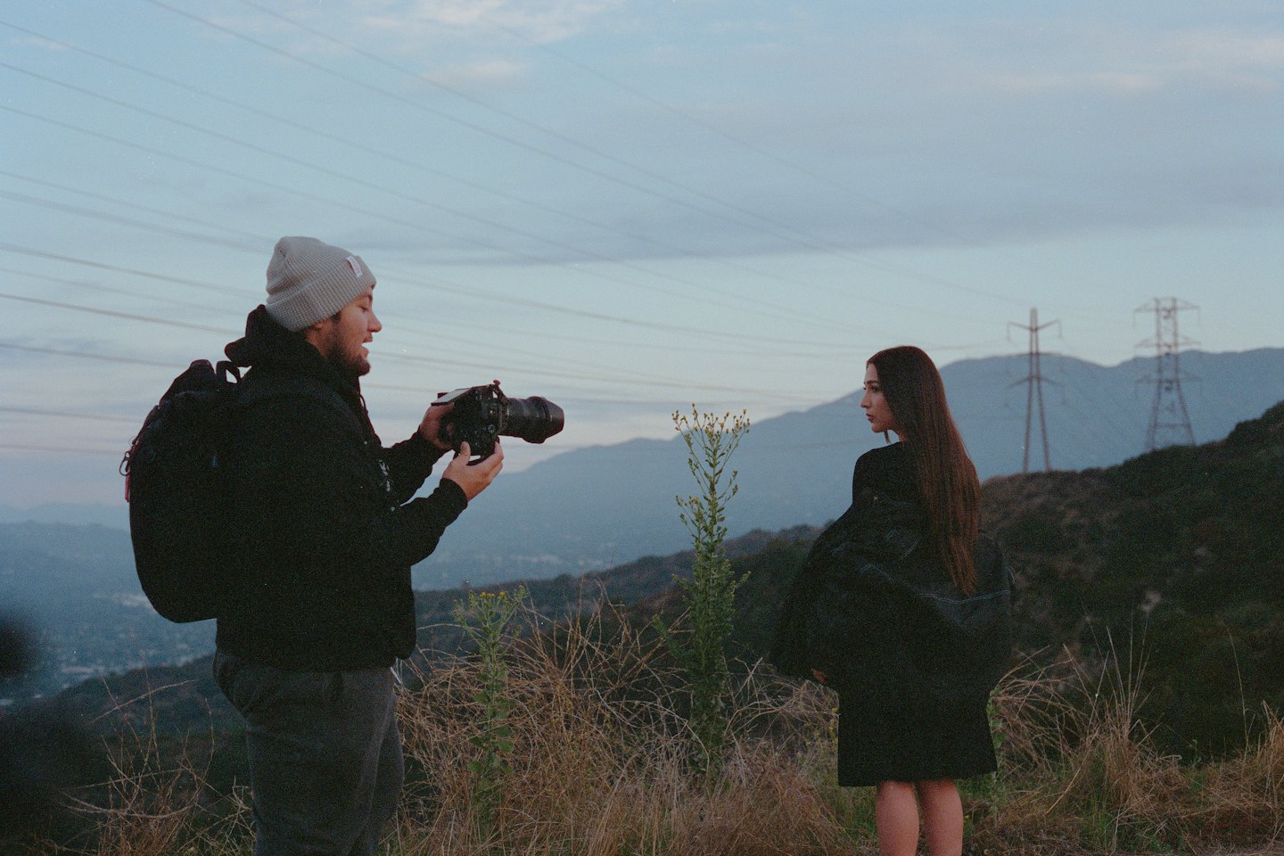 Fotografo che dirige una modella su una collina erbosa con montagne.