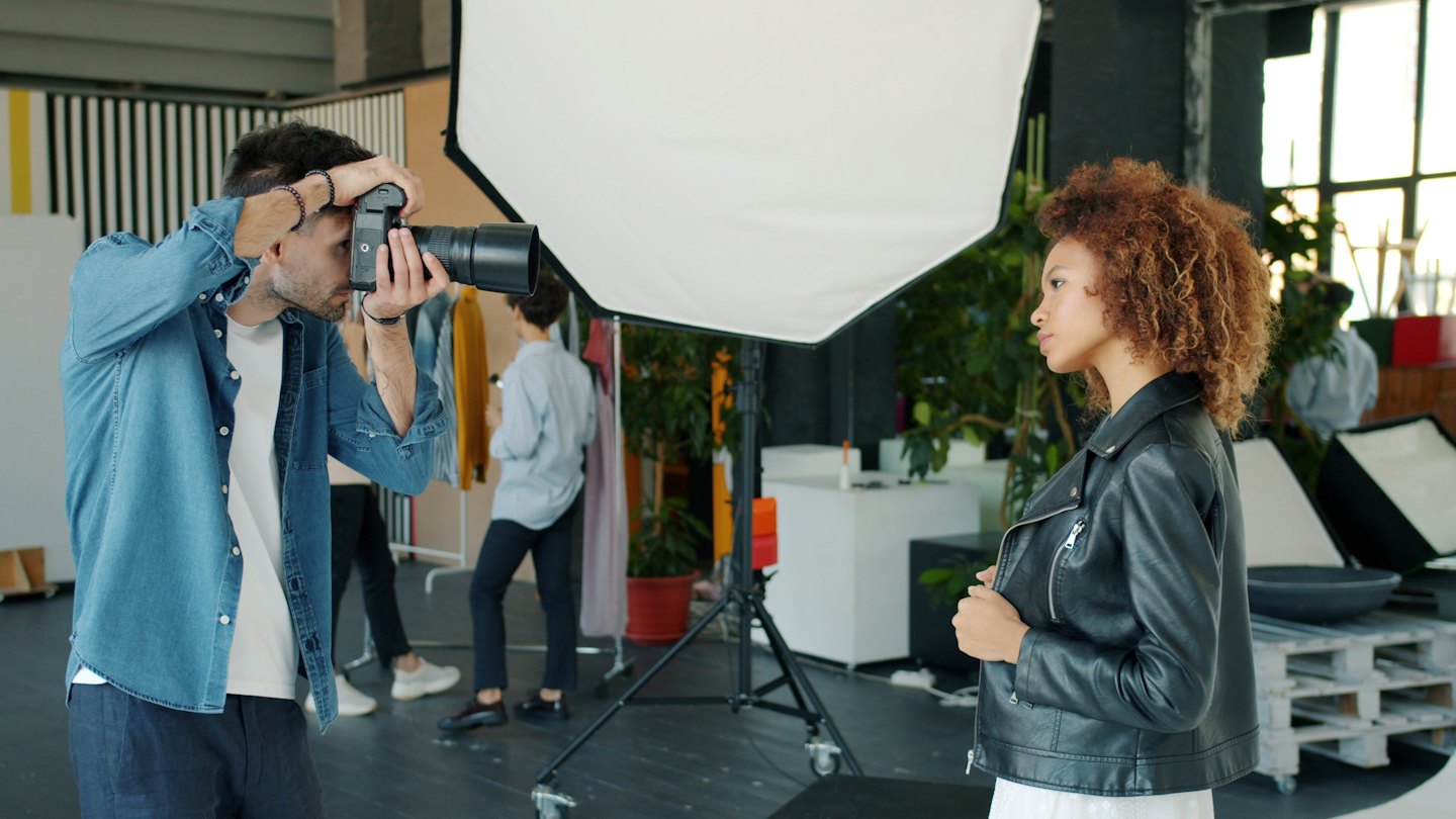 Fotografo che punta la macchina fotografica verso una modella in uno studio luminoso.