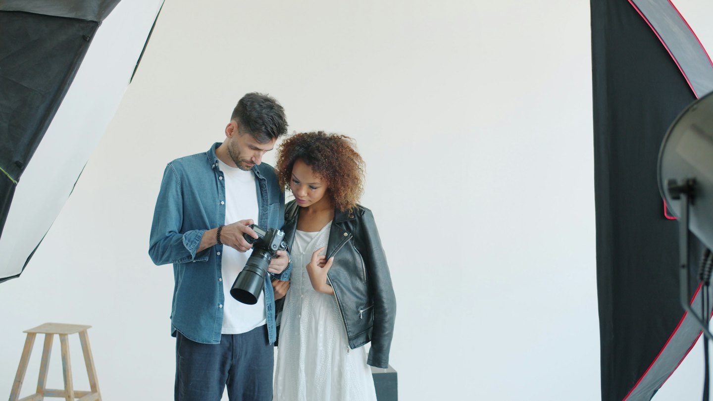 Fotografo mostra il lavoro al modello su fotocamera digitale in studio.